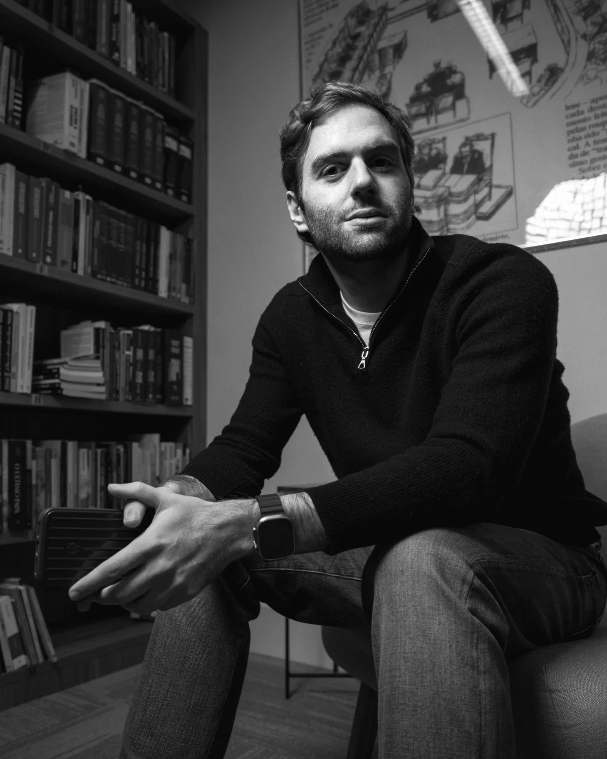 Marcello Biondi, director of NOTHING[ ], leaning forward in front of a bookshelf.